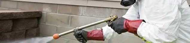 Pest control technician applying exterior insect treatment along a home foundation in Los Angeles, CA