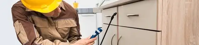Roach exterminator applying treatment under kitchen cabinets in Los Angeles, CA
