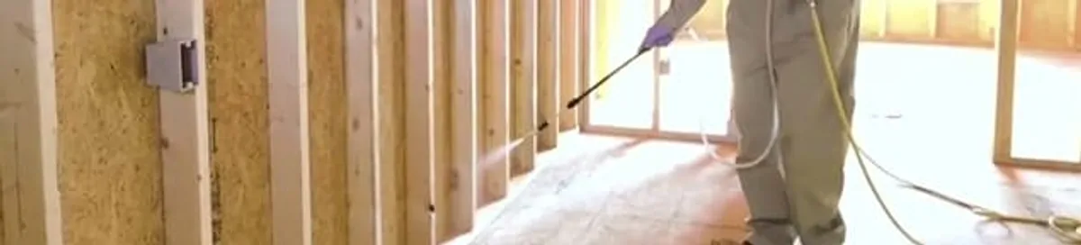Termite treatment technician applying spray along framing and unfinished walls in Los Angeles, CA