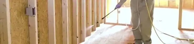 Termite treatment technician applying spray along framing and unfinished walls in Los Angeles, CA